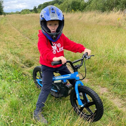  boy sat on a blue 16" storm balance bike in a field